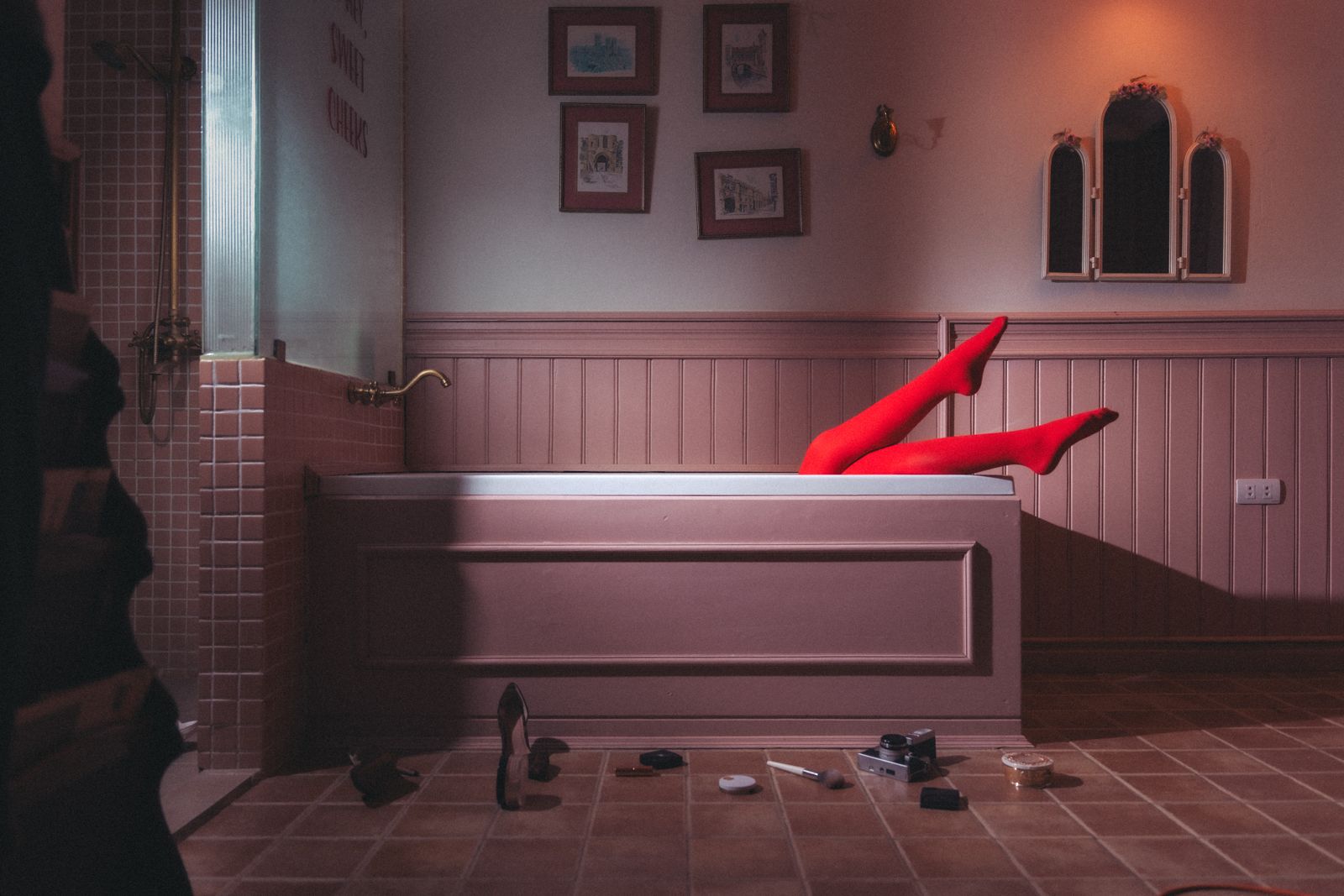 Legs in red tights rising from a bathtub in a pink-tiled bathroom